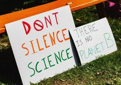 Two signs on the ground, one reads "Don't silence science" and the other says "There is no Planet B" Two signs on the ground, one reads "Don't silence science" and the other says "There is no Planet B"